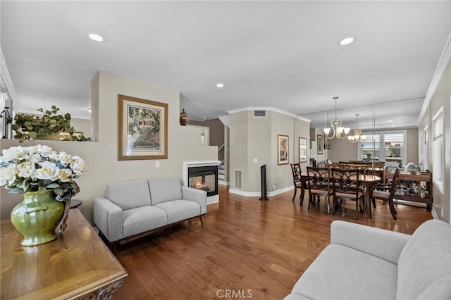living room featuring ornamental molding, a multi sided fireplace, wood finished floors, recessed lighting, and a chandelier