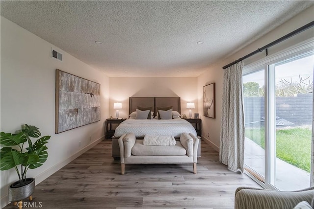 bedroom with a textured ceiling, access to exterior, wood finished floors, and baseboards