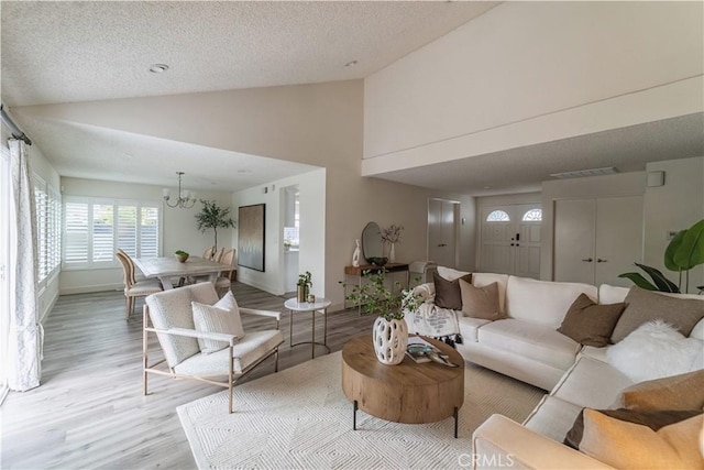 living room featuring light wood finished floors, a chandelier, a textured ceiling, high vaulted ceiling, and baseboards