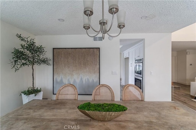 dining space featuring a chandelier, a textured ceiling, and wood finished floors