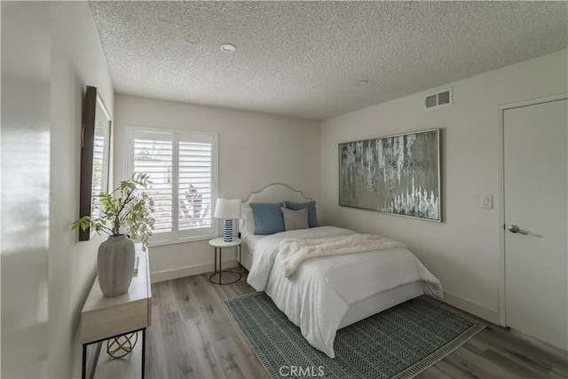 bedroom featuring wood finished floors, a textured ceiling, and baseboards