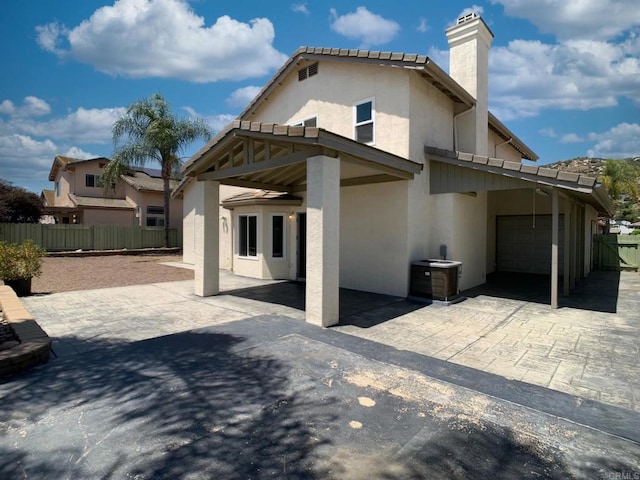 back of house with stucco siding, fence, a chimney, driveway, and a garage