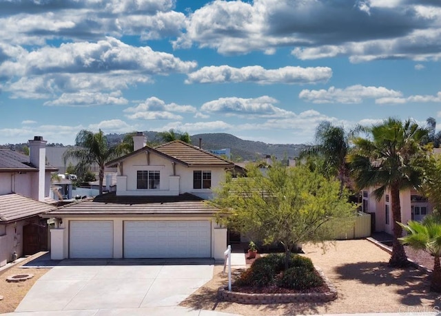 view of front of home featuring a garage, stucco siding, driveway, a chimney, and a mountain view