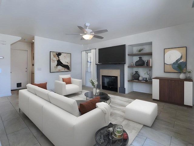 living area with built in features, a glass covered fireplace, and ceiling fan