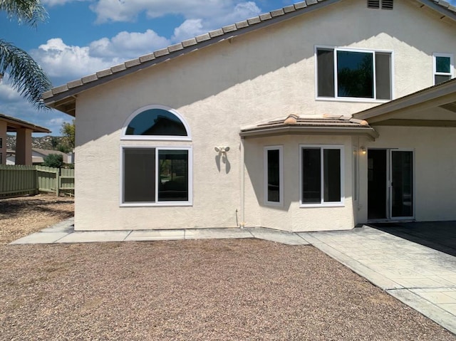 rear view of property with fence, stucco siding, a patio, and a tiled roof