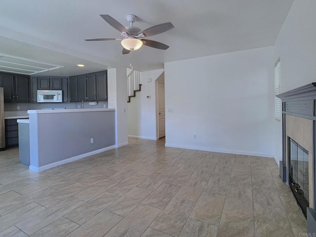 unfurnished living room featuring ceiling fan, a tile fireplace, baseboards, and stairway