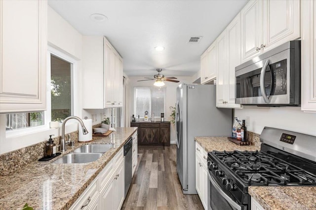 kitchen featuring appliances with stainless steel finishes, a sink, light wood-style flooring, white cabinetry, and light stone counters