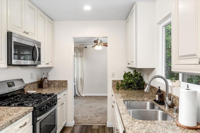 kitchen with stainless steel appliances, a sink, a ceiling fan, dark wood-type flooring, and light stone counters