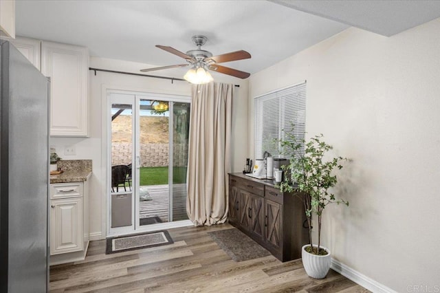 doorway featuring light wood-type flooring, a ceiling fan, and baseboards