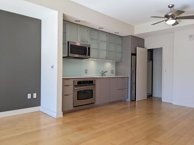 kitchen with stainless steel appliances, gray cabinetry, ceiling fan, and light wood-style floors