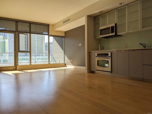 kitchen with stainless steel appliances, light wood-style flooring, gray cabinetry, and baseboards