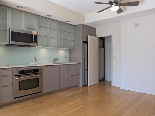 kitchen featuring stainless steel appliances, gray cabinets, light countertops, and light wood-style flooring