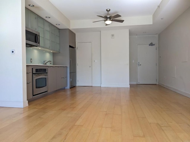 kitchen with appliances with stainless steel finishes, gray cabinetry, ceiling fan, light wood-type flooring, and baseboards