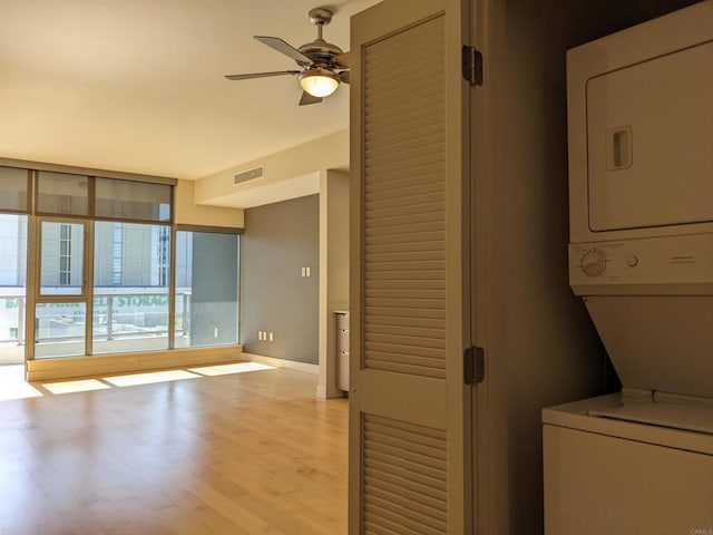 laundry area with stacked washer / drying machine, light wood-style floors, a ceiling fan, and baseboards