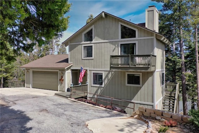 chalet / cabin featuring a chimney, a balcony, an attached garage, driveway, and stairs