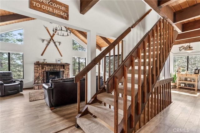 staircase featuring beamed ceiling, plenty of natural light, wood-type flooring, a fireplace, and high vaulted ceiling