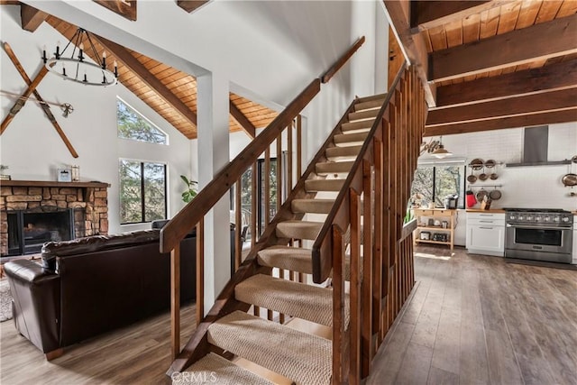 stairs with healthy amount of natural light, beamed ceiling, hardwood / wood-style floors, wood ceiling, and a fireplace