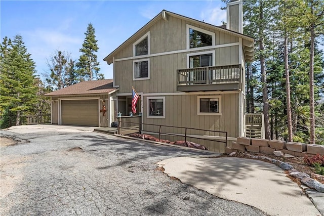 rustic home with a balcony, a garage, a chimney, and asphalt driveway