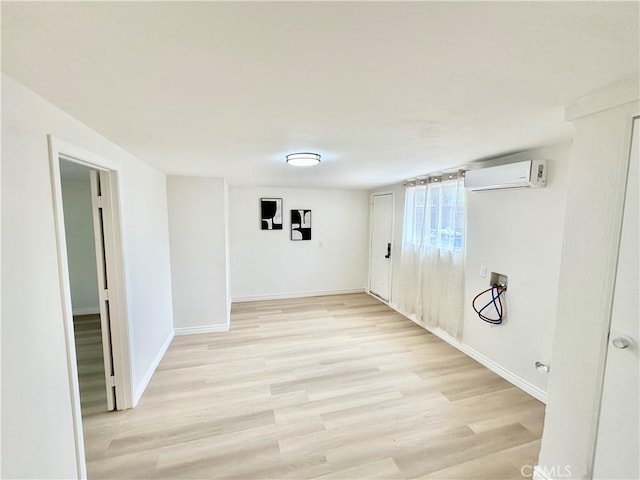 basement featuring light wood-type flooring, baseboards, and an AC wall unit