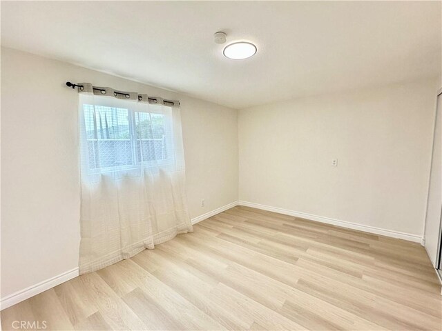 unfurnished room with light wood-type flooring, baseboards, and a smoke detector