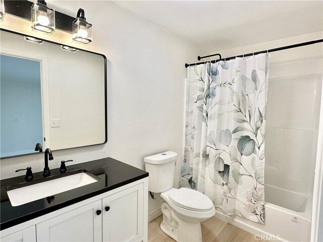 bathroom featuring wood finished floors, toilet, shower / bath combo, and vanity
