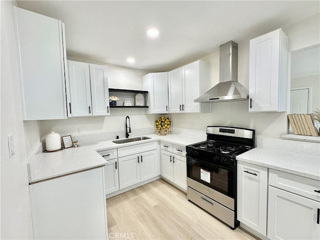 kitchen featuring a sink, wall chimney exhaust hood, gas range, open shelves, and light wood finished floors