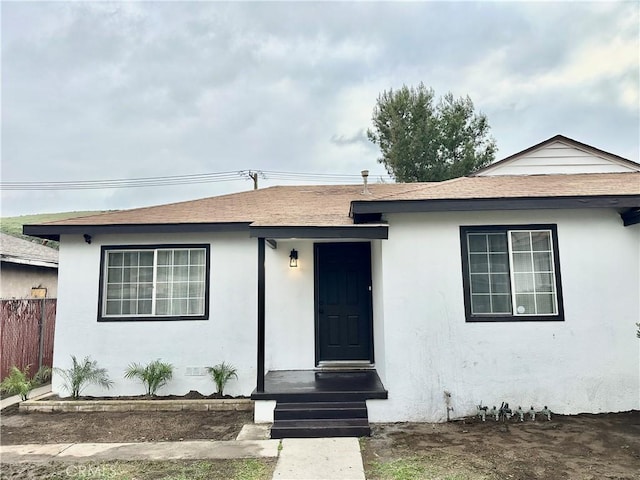 view of front of house featuring fence, roof with shingles, and stucco siding