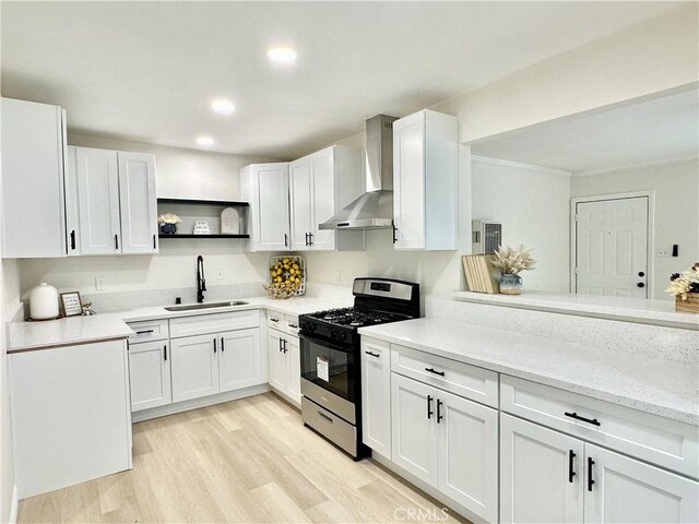 kitchen featuring stainless steel gas range, a sink, wall chimney exhaust hood, open shelves, and white cabinets