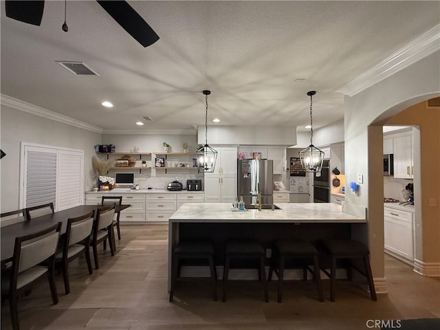 23 Ponte Sonata, Lake Elsinore, CA 92532 - kitchen with stainless steel appliances, crown molding, open shelves, white cabinets, and arched walkways