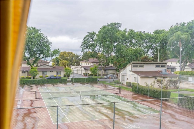 view of tennis court featuring fence and a residential view