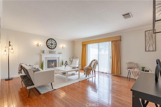 living room with light wood-type flooring, a fireplace, crown molding, and baseboards