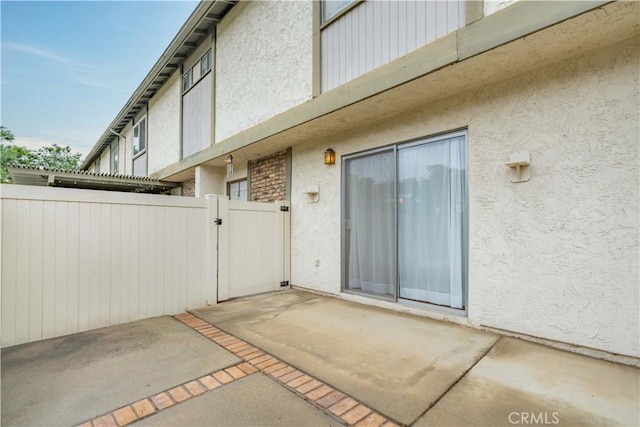 property entrance with stucco siding, a gate, a patio, and fence