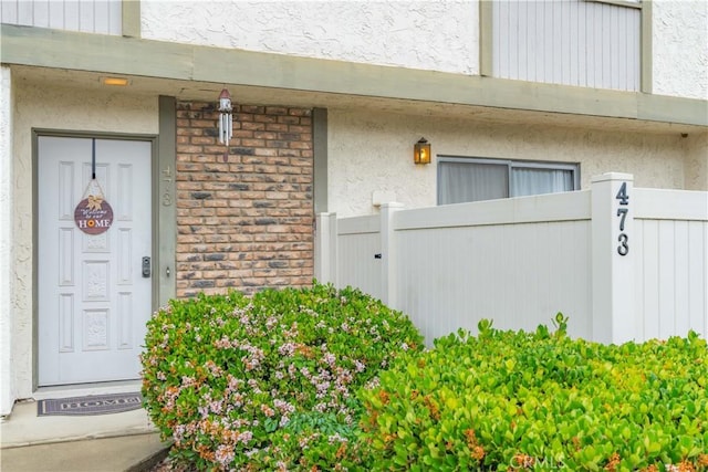 view of exterior entry with stucco siding and fence