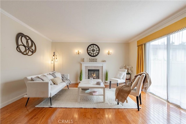 living room featuring light wood finished floors, crown molding, a tiled fireplace, and baseboards