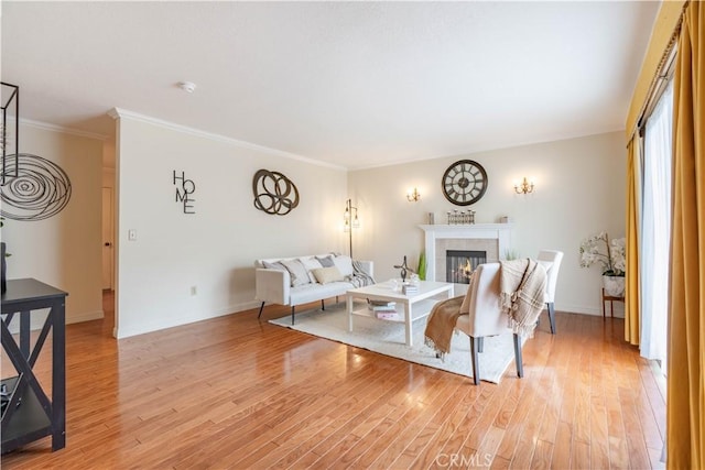 living area with a tile fireplace, light wood finished floors, ornamental molding, and baseboards
