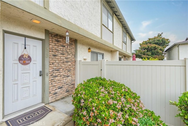 doorway to property with stucco siding, fence, and brick siding