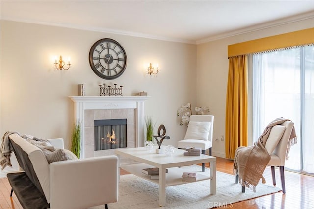 living area with a tile fireplace, ornamental molding, and light wood-style flooring