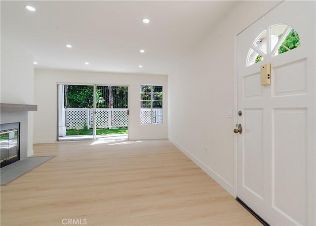 foyer featuring light wood-type flooring, baseboards, recessed lighting, and a glass covered fireplace