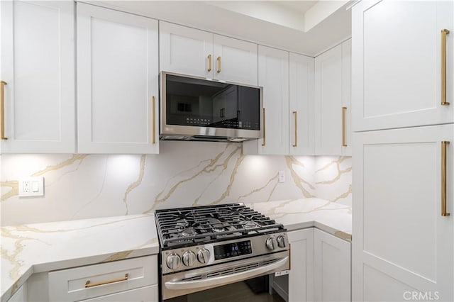 kitchen with stainless steel appliances, white cabinetry, tasteful backsplash, and light stone countertops