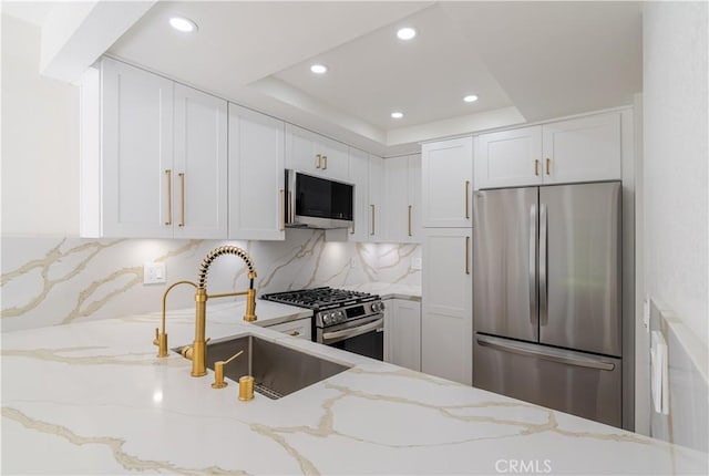 kitchen with stainless steel appliances, white cabinets, recessed lighting, light stone counters, and a tray ceiling