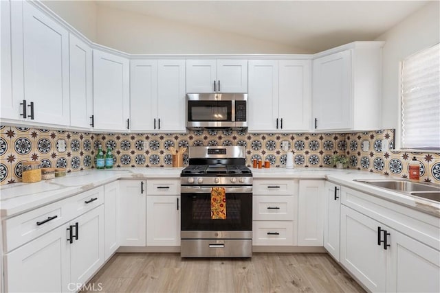 kitchen with appliances with stainless steel finishes, white cabinets, vaulted ceiling, backsplash, and light wood-style flooring