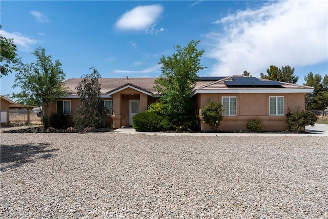 ranch-style home with roof mounted solar panels, stucco siding, and a tile roof
