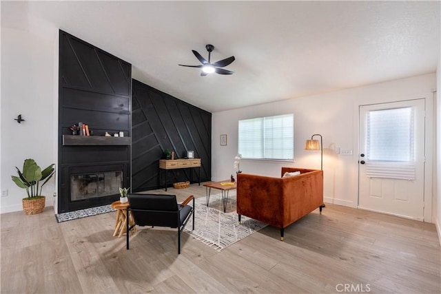 living area with a ceiling fan, wood finished floors, a large fireplace, baseboards, and lofted ceiling