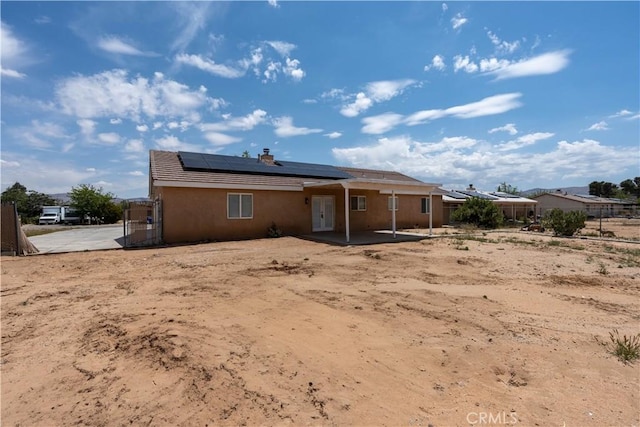 back of house featuring roof mounted solar panels, a patio area, fence, and stucco siding