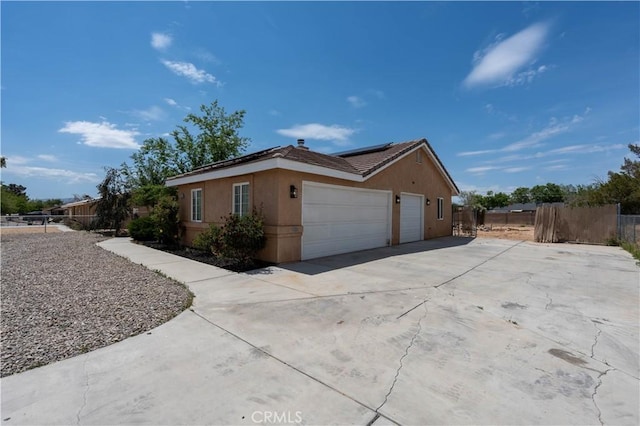 view of home's exterior with solar panels, stucco siding, a garage, driveway, and fence