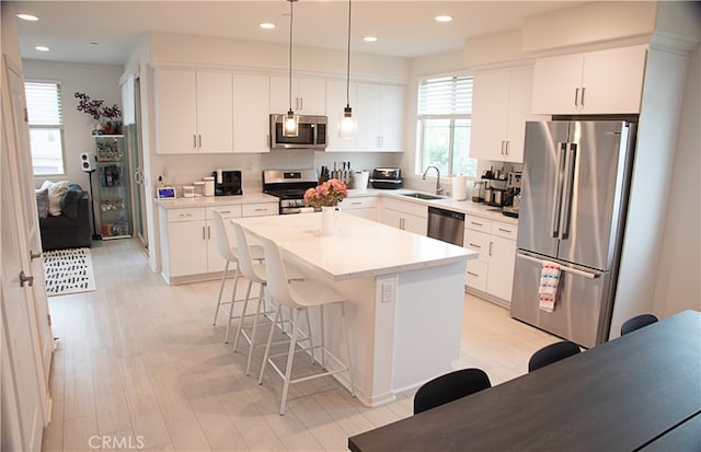 kitchen featuring appliances with stainless steel finishes, a kitchen bar, a sink, a center island, and light wood-style floors