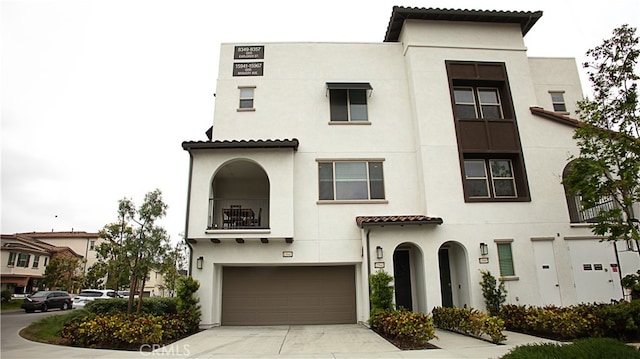 view of front facade with stucco siding, a balcony, an attached garage, driveway, and a tile roof