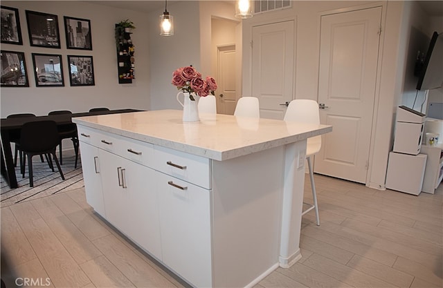 kitchen featuring a center island, a kitchen breakfast bar, pendant lighting, white cabinets, and light wood-style floors