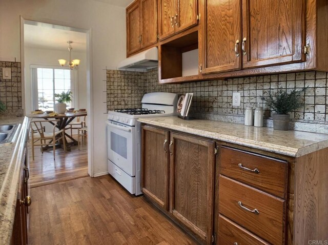 kitchen with white range with gas stovetop, under cabinet range hood, dark wood-style floors, decorative backsplash, and light countertops