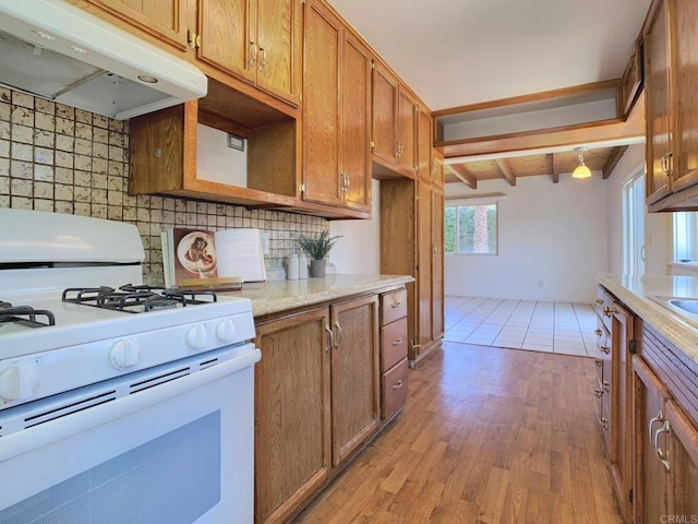 kitchen with white gas stove, under cabinet range hood, backsplash, light wood-type flooring, and beam ceiling
